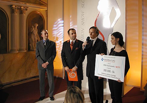 Dr. Bician prevzal symbolický šek na sumu 300 000 Sk z rúk Dr. Lopašovského, generálneho riaditeľa spoločnosti Janssen-Cilag a Johnson and Johnson Company na European Fasion Show Slovakia 2004.